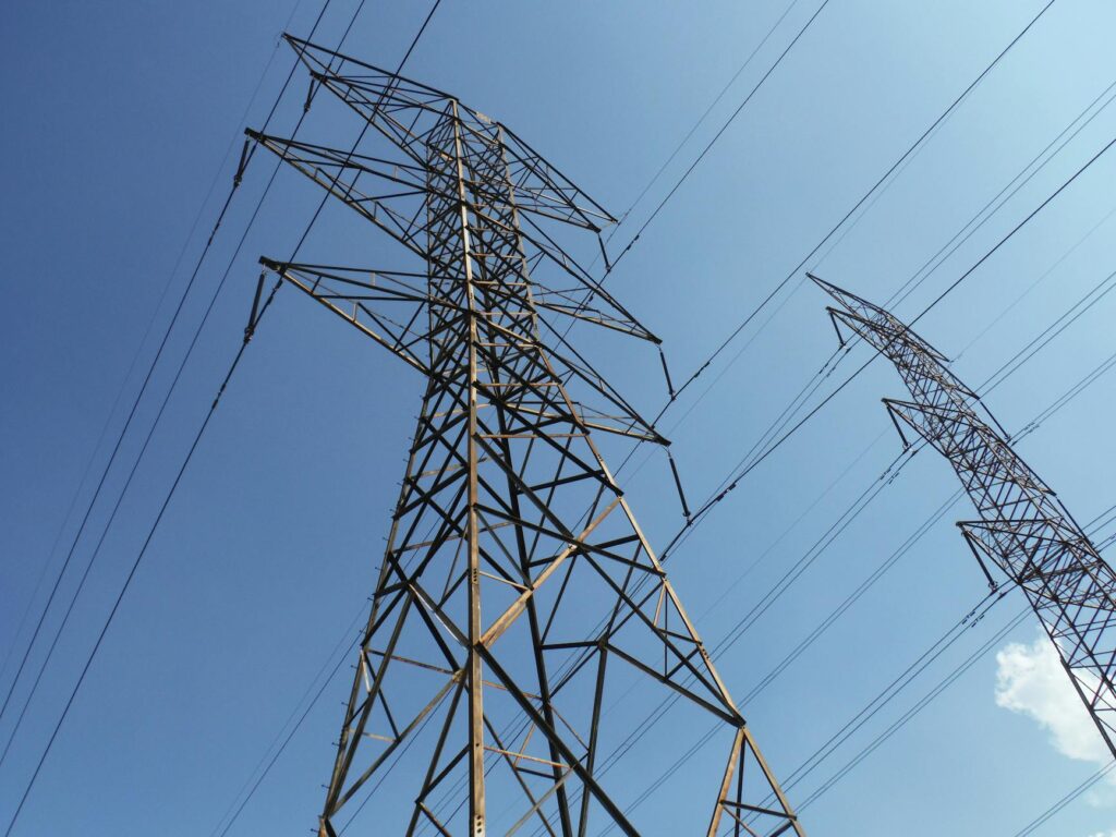 Low angle view of towering electrical transmission lines and pylons under a clear blue sky, conveying energy and electricity concepts.